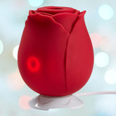 A Rose Clitoral Stimulator with Air-Pulse Suction from Cloud 9, shaped like a red rose with a glowing red circular button on a white base, is set against a soft, blurred background featuring bokeh circles. This elegant stimulator also includes a power cord extending from the base.
